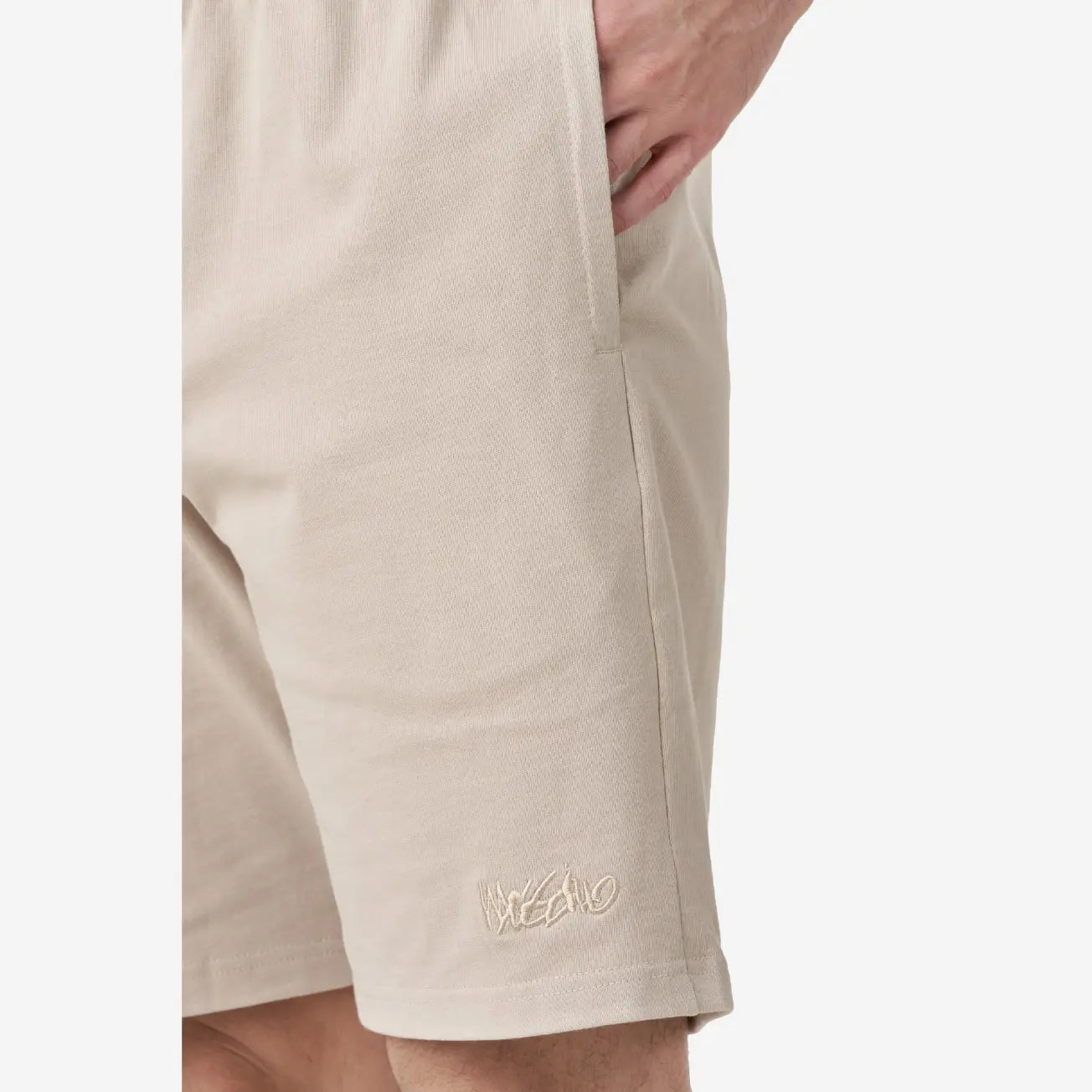 Close up view of beige casual shorts with a small embroidered logo on the lower-left side.